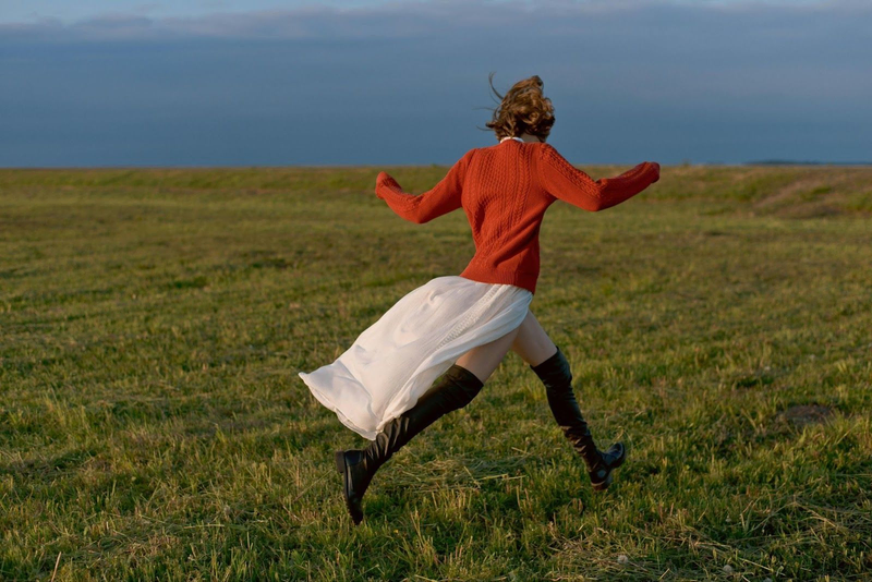 Woman in red sweater running freely across open field