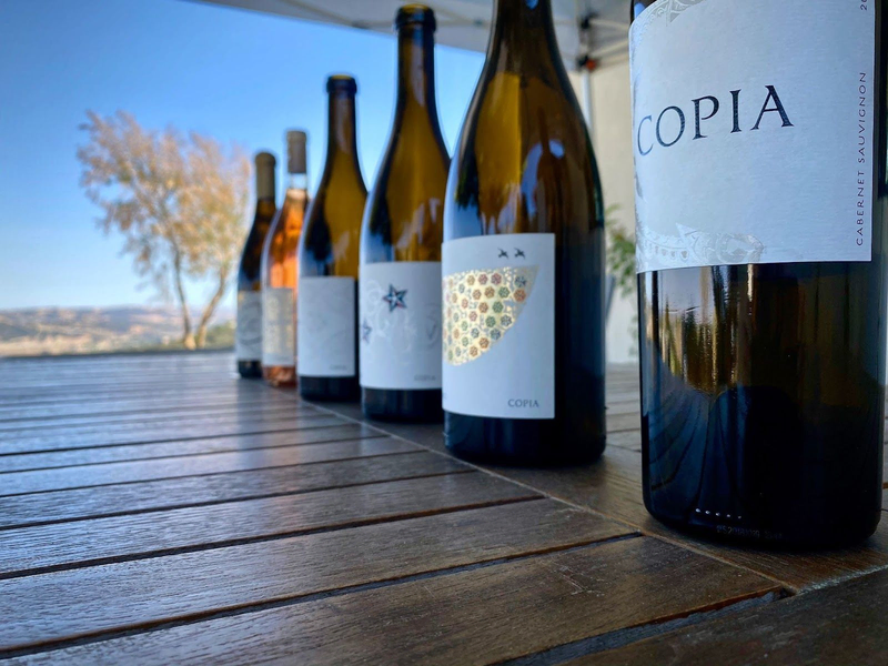 Copia Vineyards wine bottles lined up on a wooden table.