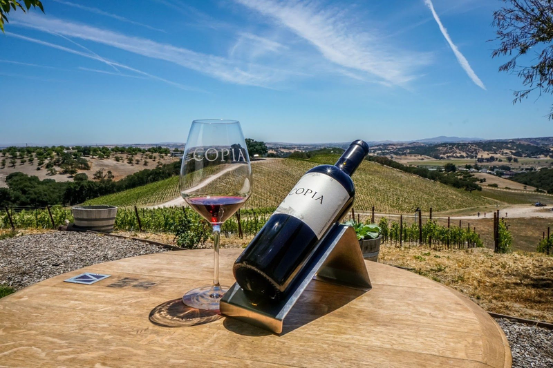 Copia wine and glass on a table overlooking vineyard hills.